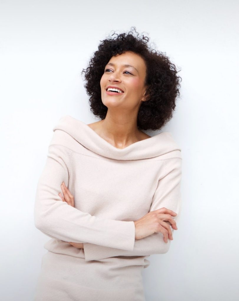 Middle-age woman with glowing skin, white smile and curly hair. Emsella Chair Page Aviva Med Spa Centennial CO